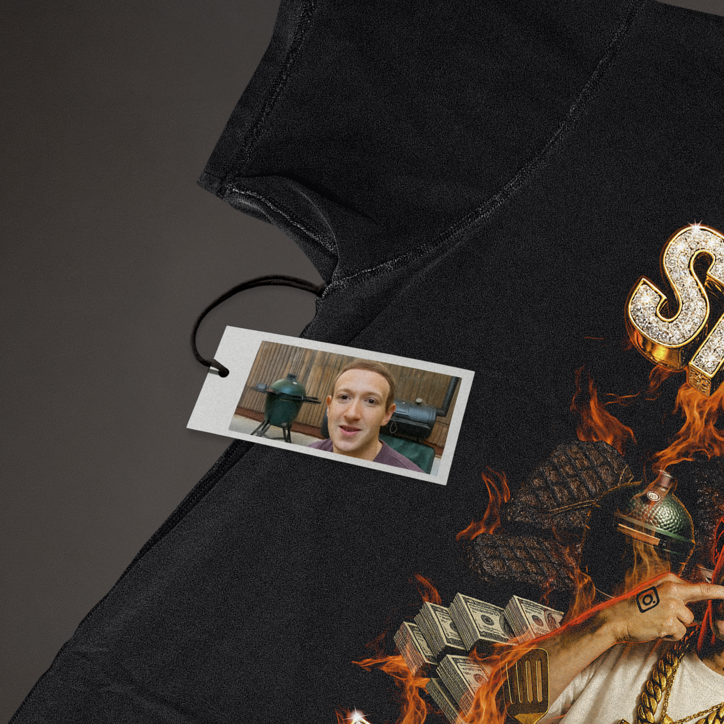 Close-up of Smoking Meats t-shirt graphic with flames and dollar bills, featuring hang tag showing Mark Zuckerberg's face and two BBQ smokers; detail shot for product
